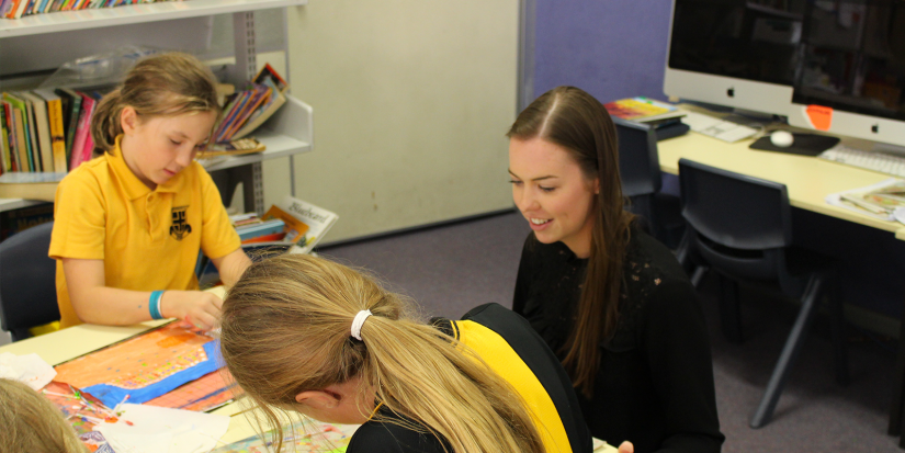 Lauren sitting next to primary students doing artwork