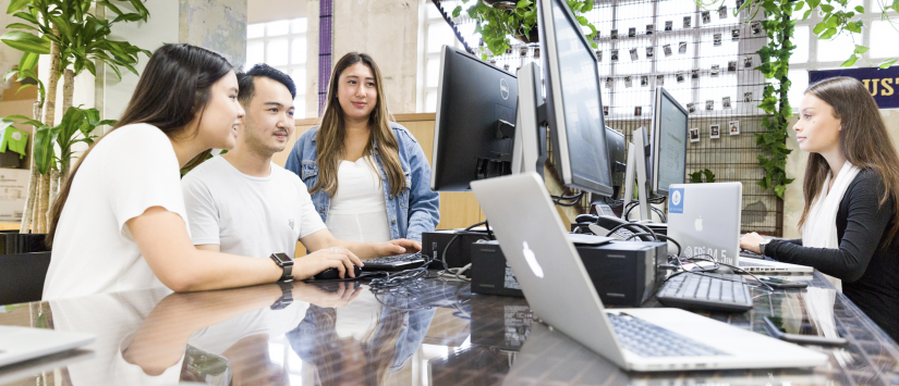 A group of students sitting at desk, looking at laptop and computer screens