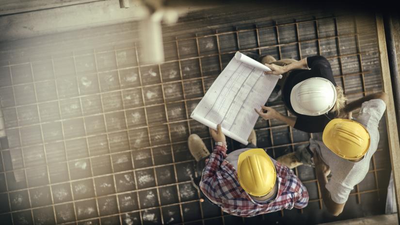 Three colleagues discuss blueprints at a worksite