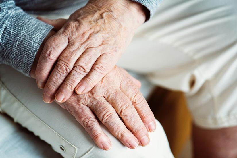 Close up of elderly person's hands, crossed over their knee.
