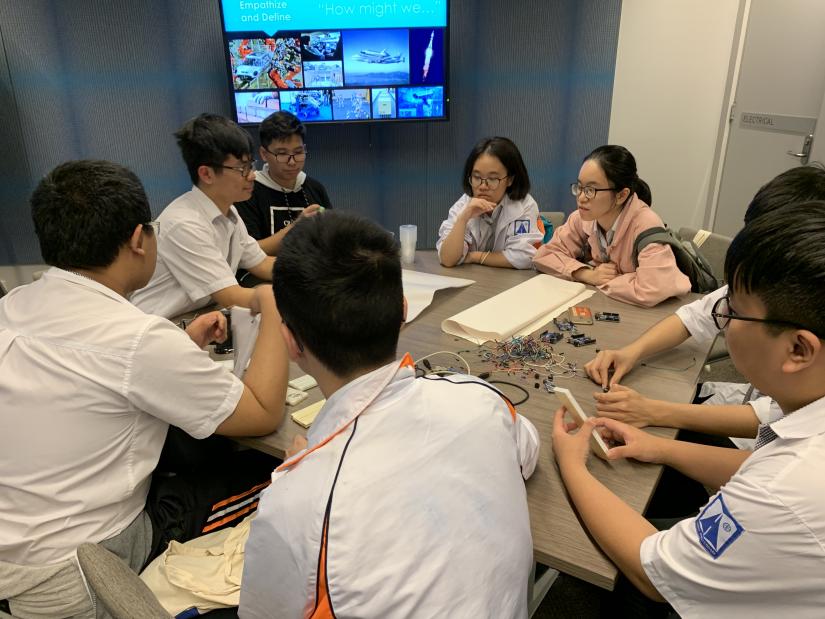 A group of students sit around a table and examine circuitry