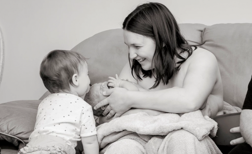 Mother holding new born with second child at home