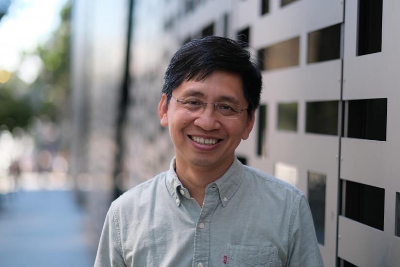 A man smiles in front of a building grille