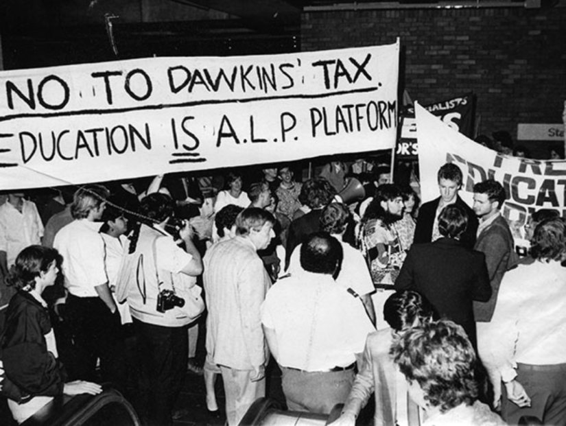 Crowd of people holding a sign "No to Dawkins tax"