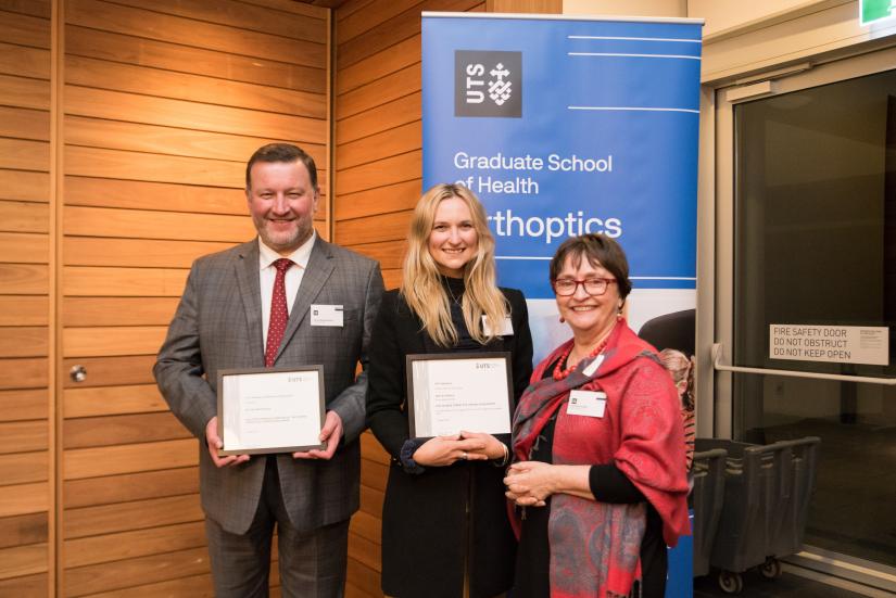 Male and two females holding certificates in front of Orthoptics banner.