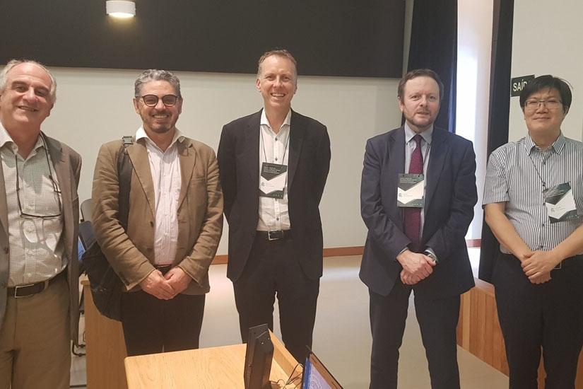 Five male academics standing in a row in a classroom