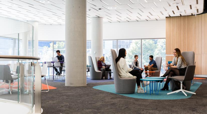 Students sit on lounges and stools around tables overlooking Alumni Green