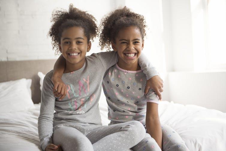 Image of two identical twin girls sitting on a bed with arms around each other