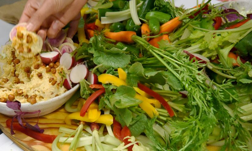 Vegetables on a cutting board with a hand scooping dip from a bowl