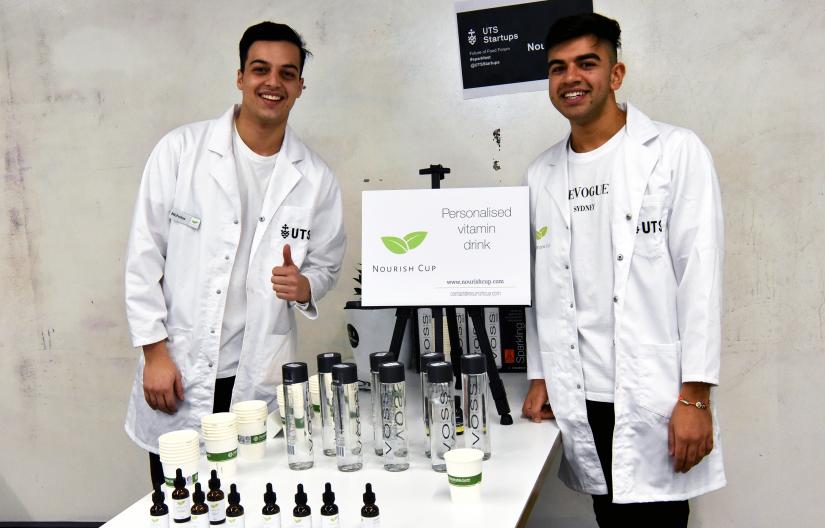 Two students from the UTS startup Nourish Cup beside a table with their products on display