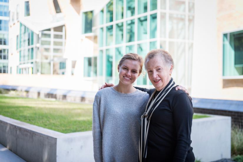 Laurie Cowled and Ellie Slade facing the camera with their arms around each other in front of Building 8