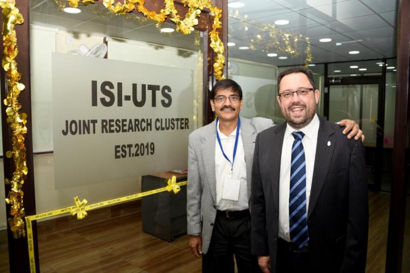 Two men stand in front of a plaque