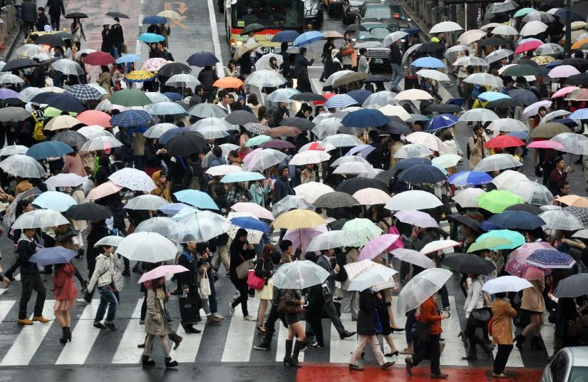 Crowds carrying umbrellas cross a city street