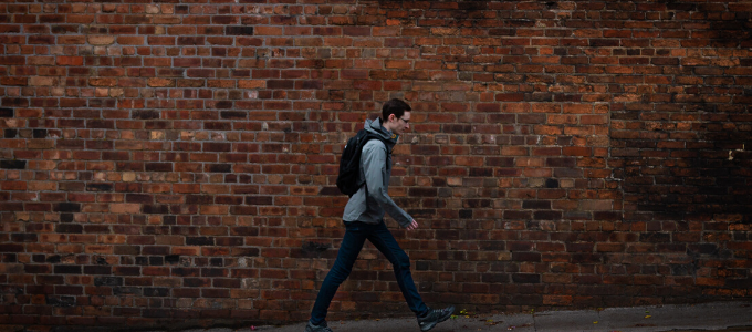 Lonely man with backpack walking on street with brick background.