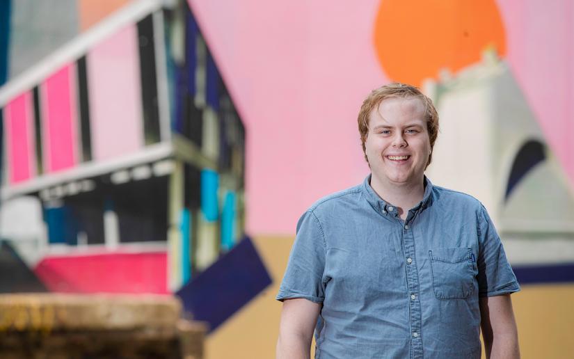 Young man stands in front of pink mural