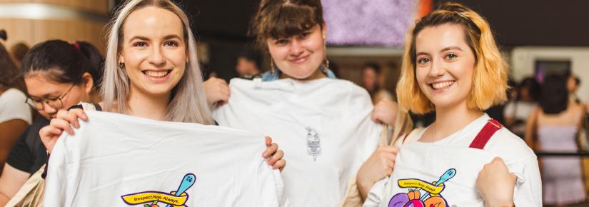 Three students hold up t-shirts with the Respect.Now.Always campaign branding.