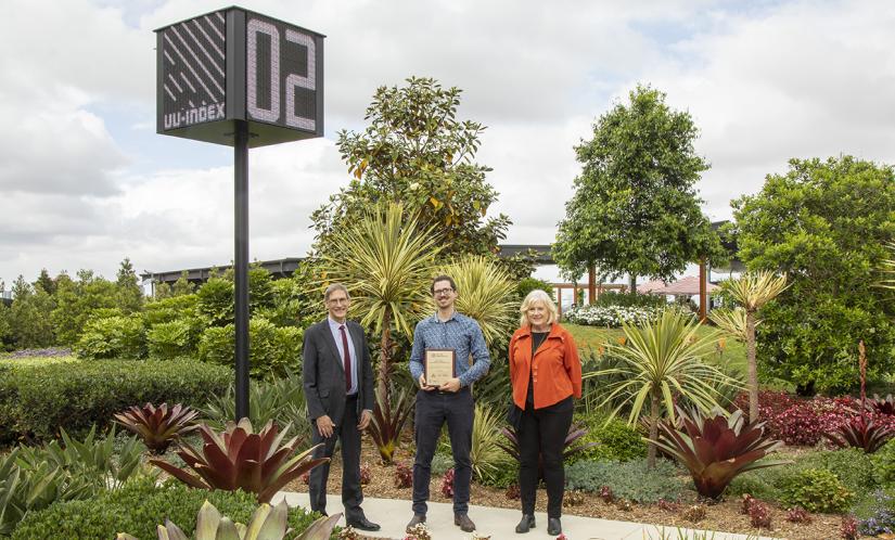 Three people stand under a high-tech sensor that measures the environment