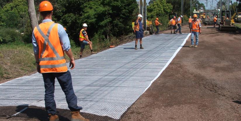 Workers in hi vis gear using geo-composite to stabilise rail track