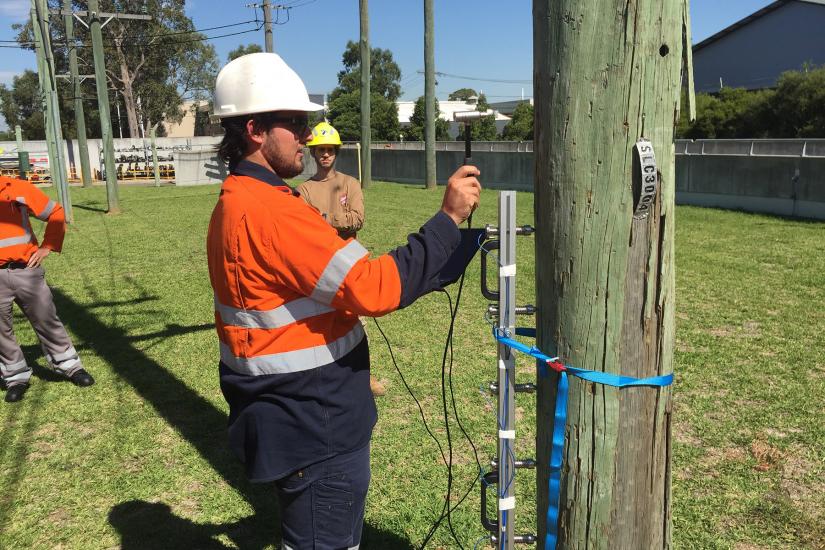 Man in hard had holds a device against a telegraph pole