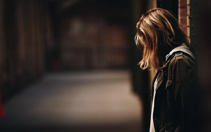 Woman in a dark hallway hangs her head.