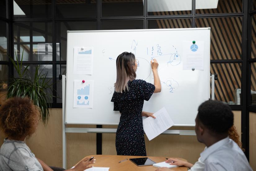 Woman writing on whiteboard with two people watching