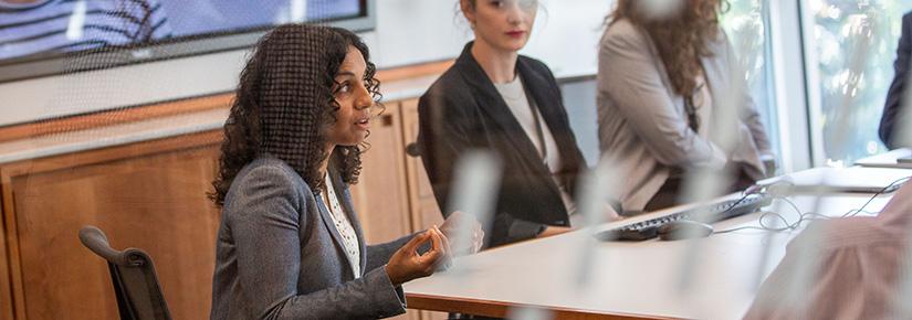 A view of a boardroom meeting, in which 3 women are visible