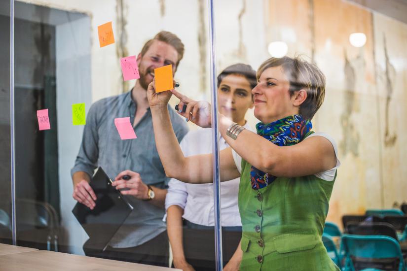 People writing on sticky notes and sticking them on a glass wall