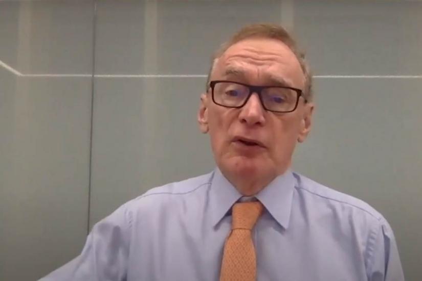 A man in a blue shirt and a pink tie is speaking on Zoom.