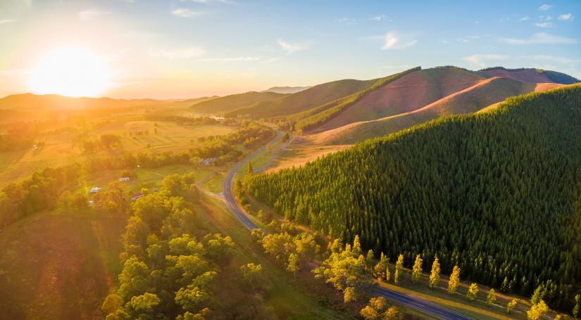 Green hills in the foreground with a blue sky and sun coming over the horizon