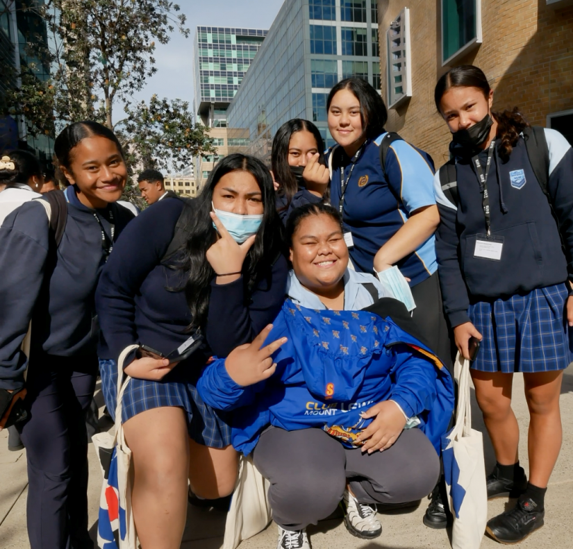 group photo of high school girls sitting together outside, smiling at the camera