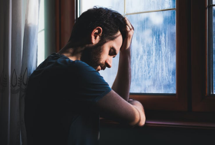 Man with head in hand leaning against a window