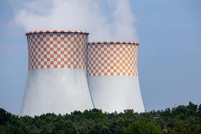 Two chimney stacks smoking with blue sky and trees in foreground