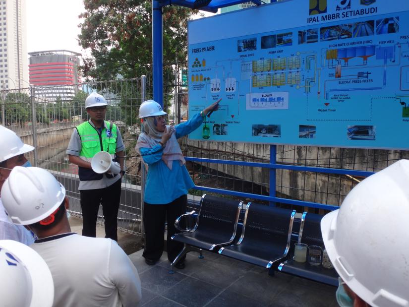 A woman in a hard hat pointing at a blue sign next to a man in a green high-visibility vest.