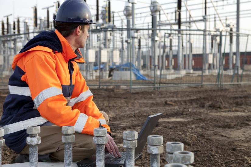 A man in a high-visibility jacket squatting down at a power station