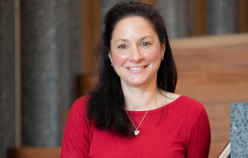 Woman with medium length dark hair smiling and looking at the camera in a red top