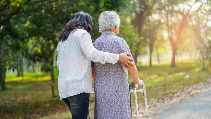 Woman helping elderly person walk outdoors