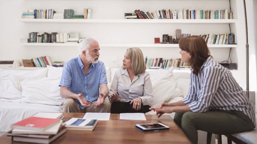elderly man and woman on sofa talking to younger woman