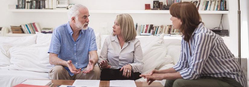 elderly man and woman on sofa talking to younger woman