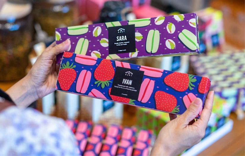 Womans hands holding two boxes of colourful boxes of macarons with the stories of two victims of modern slavery as part of the Humanmart shop in Oxford Street Sydney