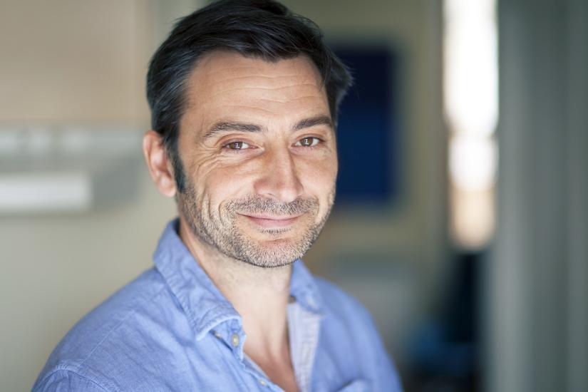 Tired but smiling man with dark hair wearing blue buttoned shirt