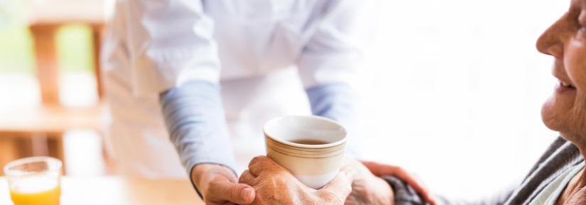 Elderly woman in aged care has help holding a cup