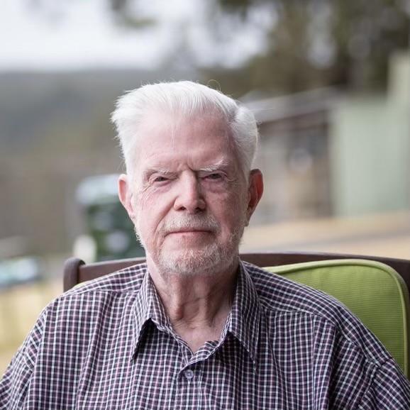 Jack Greenland head and shoulders shot, seated outside with blurred background