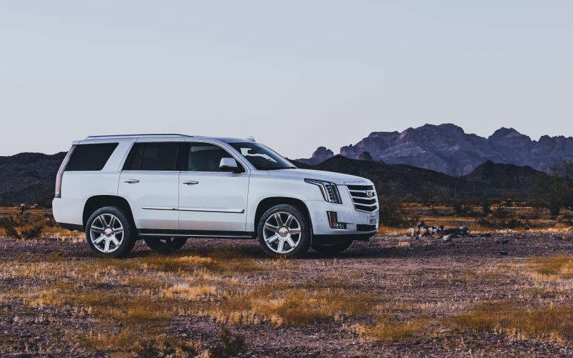 a white SUV sits on a dirt path with mountains in the background.