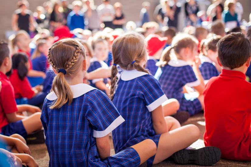 A group of school children sitting on the ground looking forward