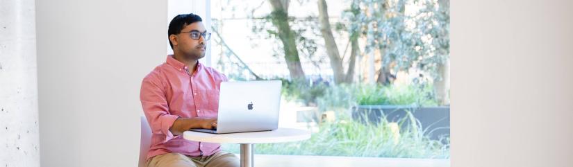 Student sitting at a laptop looking into the distance