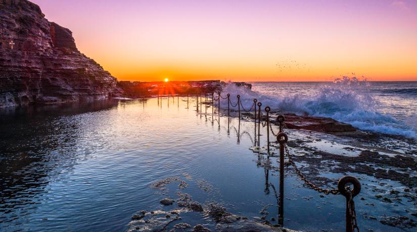 A pink sky at sunrise with ocean pool in the foreground.