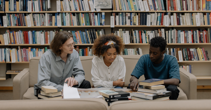 Three students sit down reading books in a library