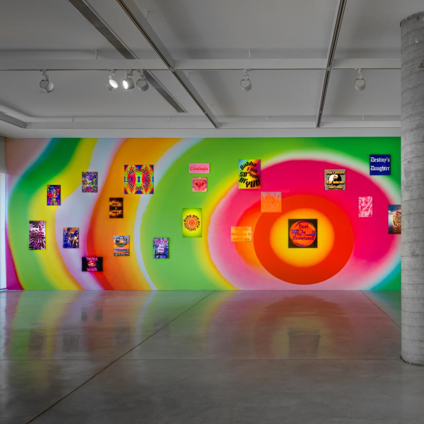 A rainbow wallpaper covers the whole wall of an art gallery. Multiple smaller posters are scattered over the surface.
