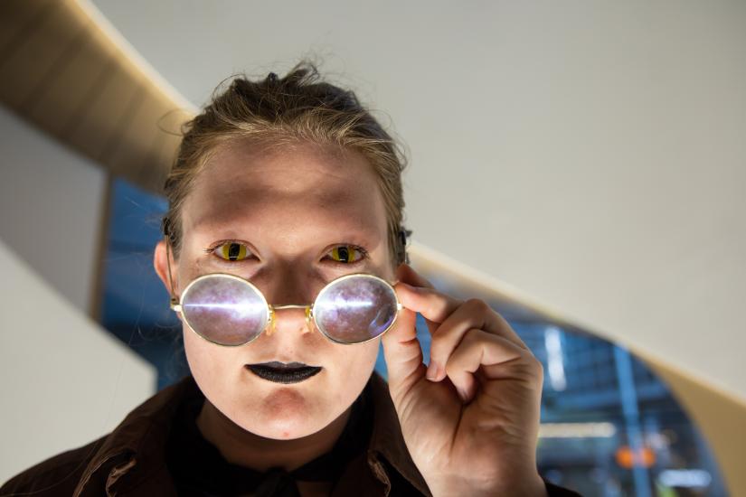 A person with glasses, wearing black lipstick looks directly at the camera.