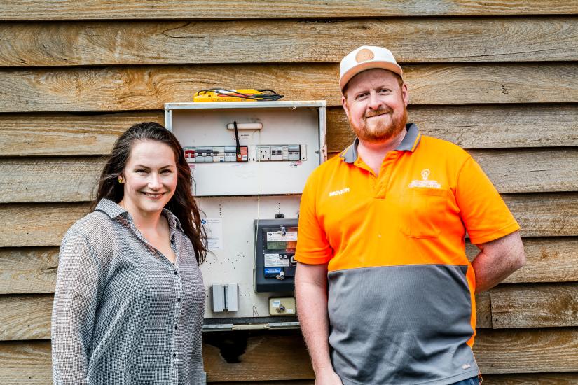 A woman with long hair is smiling and standing next to a tradesman in a bright orange and grey top